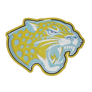 May include: An embroidered patch featuring the head of a snarling jaguar in profile. The design uses bright yellow, light blue, and white thread with a dark blue outline, showing the animal with bared teeth, whiskers, and spotted fur patterns.
