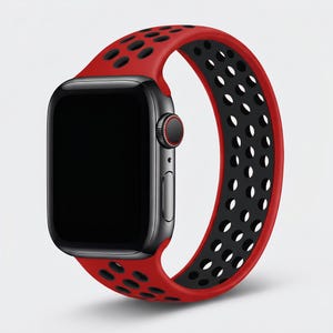 May include: A smartwatch with a black rectangular screen and a dark gray casing. The watch features a silicone band with a two-tone design, displaying a vibrant red exterior and a black interior, characterized by a pattern of circular perforations.