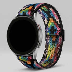 May include: A silver smartwatch with a black screen and a colorful patterned band. The band features a geometric design with a mix of bright colors including red, yellow, blue, and green. The watch is shown against a light gray background.