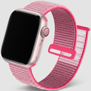 May include: A smartwatch with a light pink metallic casing and a black screen. The watch features a vibrant pink woven nylon sport loop band with a matching pink plastic fastener and a side crown with a thin red accent ring around the edge.