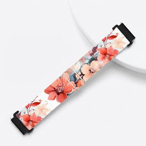 May include: A watch band featuring a vibrant floral pattern with coral, peach, and soft blue petals against a white background. The strap includes a metallic rose gold adjustable slider and black connectors at both ends for secure attachment.