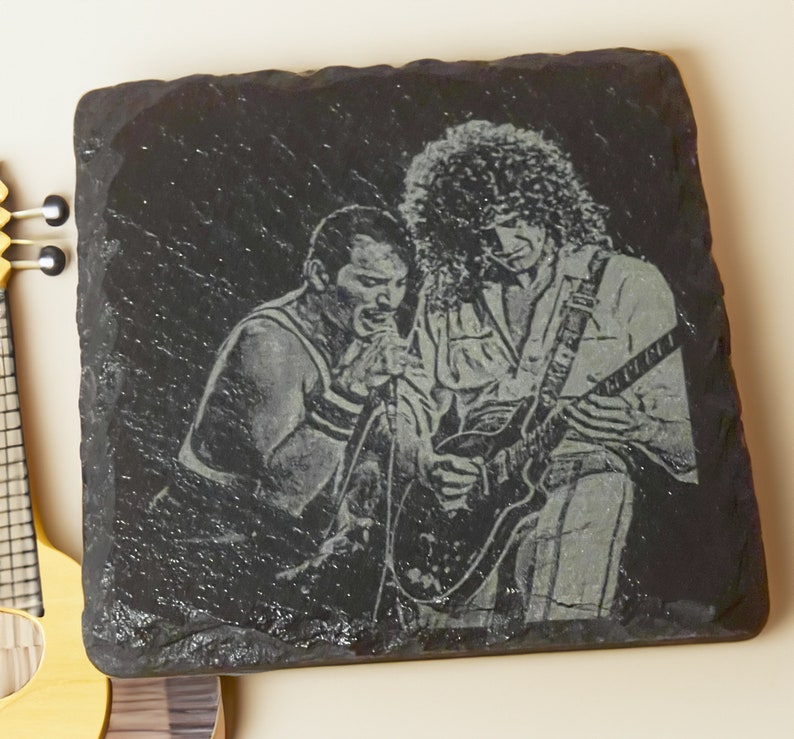 May include: Black and white engraved image of two musicians on a black slate coaster. The musician on the left is singing into a microphone and the musician on the right is playing an electric guitar.
