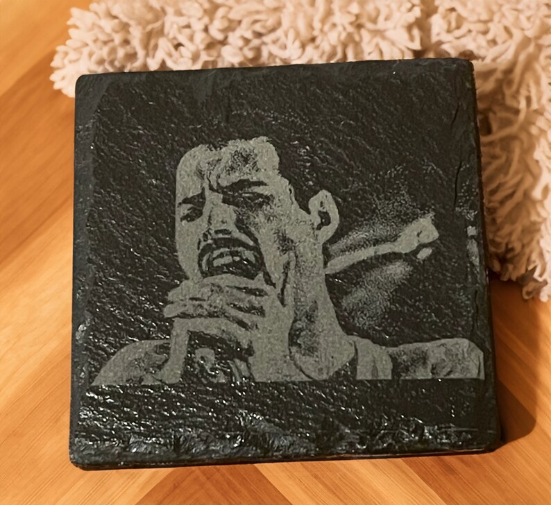 May include: A black slate coaster with a white engraved image of a person singing into a microphone.