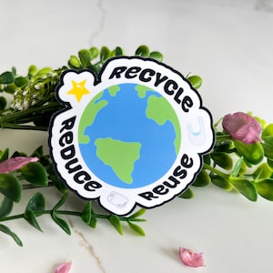 May include: A white sticker with a blue and green globe in the center. The globe is surrounded by the words "Reduce", "Recycle", and "Reuse" in a circular pattern. A yellow star and a white silhouette of a toilet paper roll are also on the sticker.