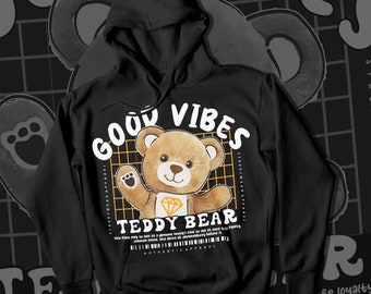 May include: Black hoodie with a graphic of a teddy bear wearing a diamond necklace. The graphic is surrounded by a grid pattern and the text "Good Vibes Teddy Bear" is printed above the bear. The text "Streetwear Apparel" is printed on the sides of the graphic.