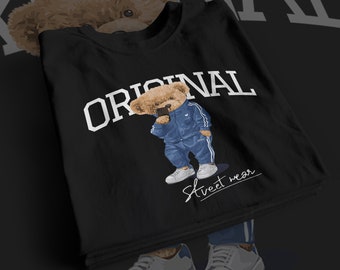 May include: Black t-shirt with the word "ORIGINAL" in white block letters. The shirt features a cartoon teddy bear wearing a blue tracksuit and white sneakers. The words "Street wear" are written in cursive.