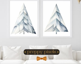 May include: Two framed watercolor prints featuring abstract blue and white Christmas trees. The artwork has a geometric design and is set against a white background. The prints are displayed above a white sofa. The text "preppy pixels" is on a brown banner.