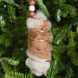 May include: A handmade Christmas ornament featuring a spiral of copper wire wrapped with white and brown wool felt. The ornament is adorned with wooden beads in shades of brown and gold.