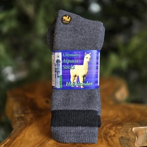 May include: Gray alpaca socks with a black stripe at the top. The socks are packaged with a label that says "Ultimate Alpaca Socks" and features a white alpaca with the text "Highlander".