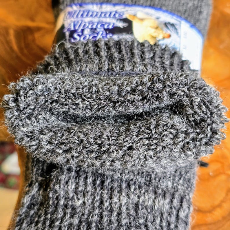 May include: Close-up of the top of a gray alpaca sock. The sock is folded over and the inside is fluffy. The label reads "Ultimate Alpaca Socks".