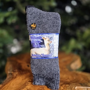 May include: Gray alpaca wool socks with a label that reads "Ultimate Alpaca Socks Extreme Thermal". The label features a white alpaca and a blue background with snowflakes.
