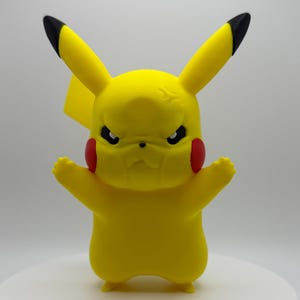 May include: A yellow Pikachu figurine with black-tipped ears, red cheek markings, and an angry expression. The figure has its arms outstretched and is standing on a white surface.