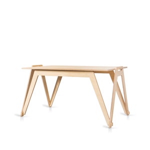 May include: A light-colored wooden desk with a minimalist design. The desk features a rectangular tabletop supported by angled, V-shaped legs. The desk is approximately 48 inches long and 24 inches wide.