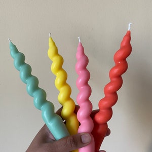 May include: Four colorful spiral candles in shades of mint green, yellow, pink, and coral. The candles have a twisted design and are held in a hand. The candles are a decorative item.