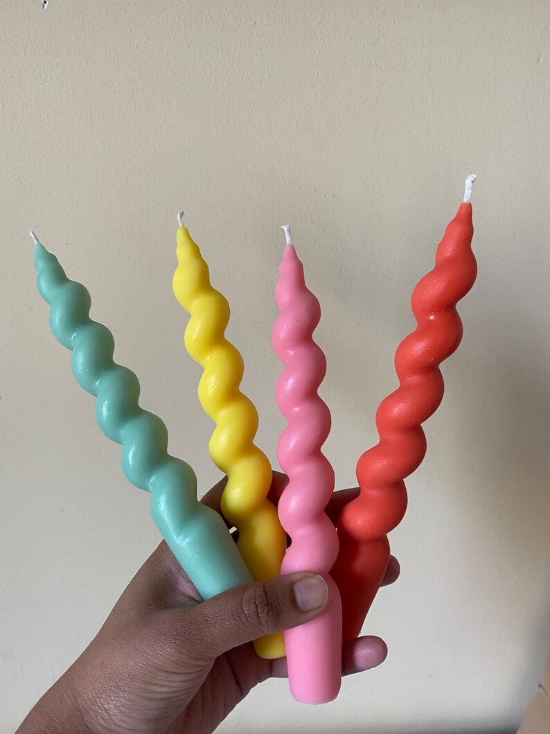 May include: Four colorful spiral candles in shades of mint green, yellow, pink, and coral. The candles have a twisted design and are held in a hand. The candles are a decorative item.