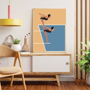 May include: A framed illustration of two women in black and white polka dot swimsuits diving off a diving board into a blue pool. The background is a light orange color.