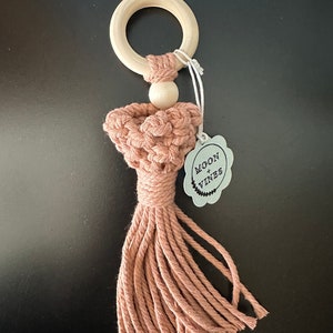 May include: A pink crocheted baby teether with a wooden ring and a wooden bead. The teether has a tassel and a tag that says "Moon + Vines".