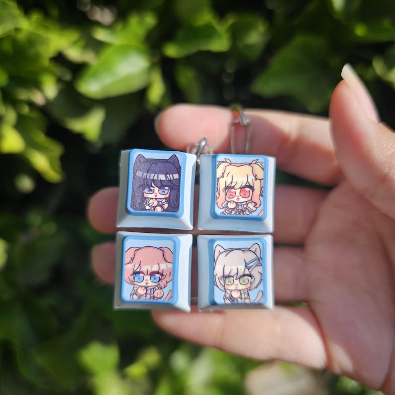 K&ouml;nnte beinhalten: Vier blaue und wei&szlig;e Keycaps mit Anime-Illustrationen von M&auml;dchen. Jede Keycap zeigt ein anderes M&auml;dchen mit einzigartigen Haaren und Kleidung.