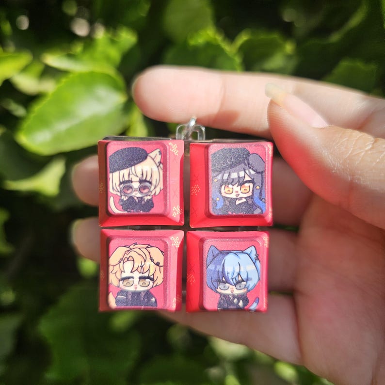 K&ouml;nnte beinhalten: Vier rote Keycap-Anh&auml;nger mit verschiedenen Anime-Charakteren. Jeder Anh&auml;nger zeigt einen anderen Charakter mit einem einzigartigen Design und Ausdruck. Die Anh&auml;nger sind an einer silbernen Kette befestigt.