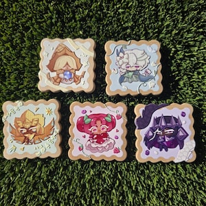 May include: Five square wooden coasters with scalloped edges, each featuring a unique anime-style character illustration. The designs include a blonde figure in a brown cloak, a white-haired character, a golden winged figure, a pink-haired character holding a heart, and a dark purple armoured character.
