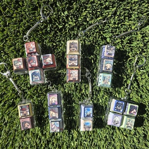 Puede incluir: Una colección de seis llaveros hechos de teclas de teclado mecánico de plástico transparente, cada una con coloridas ilustraciones de personajes estilo anime. Las teclas están dispuestas en varios grupos y unidas a anillos de metal plateado.