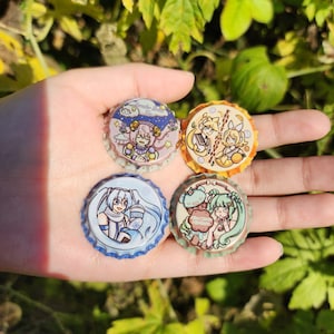 May include: Four colorful bottle cap pins featuring anime characters. The pins are round and have a white background with colorful illustrations. The text on the pins reads "Lemonade Ice", "Fruit Smoothie", and "Sweet Dreams".