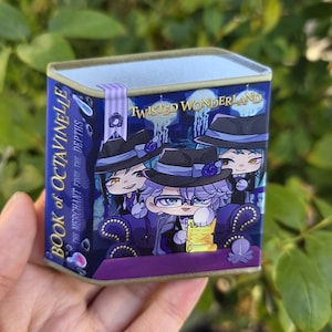 Puede incluir: Una lata rectangular con una ilustración de dibujos animados de personajes de "Twisted Wonderland". La lata es principalmente azul y morada, con el texto "Book of Octavinelle" y "The Merchant from the Depths". Los personajes llevan sombreros negros.