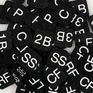 May include: A close-up of black fabric squares with white letters and numbers. The letters and numbers include: RF, US, 3F, C, 1B, CB, P, 2B, 3B, EC, SS, CF, and C.