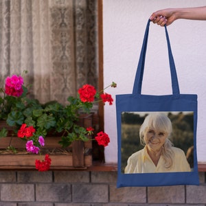 May include: A blue tote bag with a photo of an older woman with white hair smiling. The photo is on a white background.
