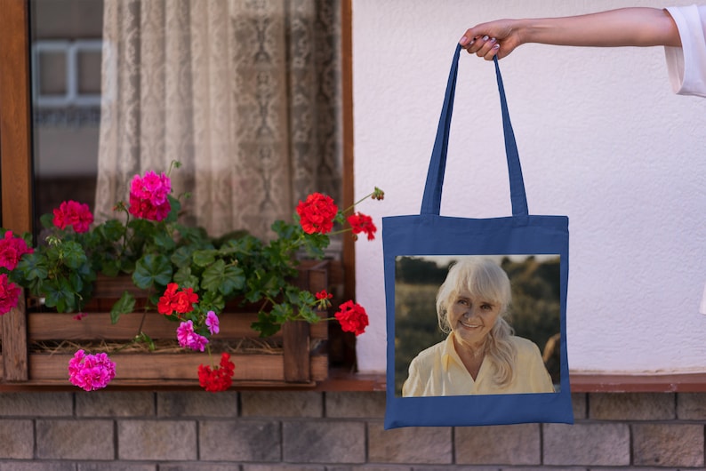 May include: A blue tote bag with a photo of an older woman with white hair smiling. The photo is on a white background.