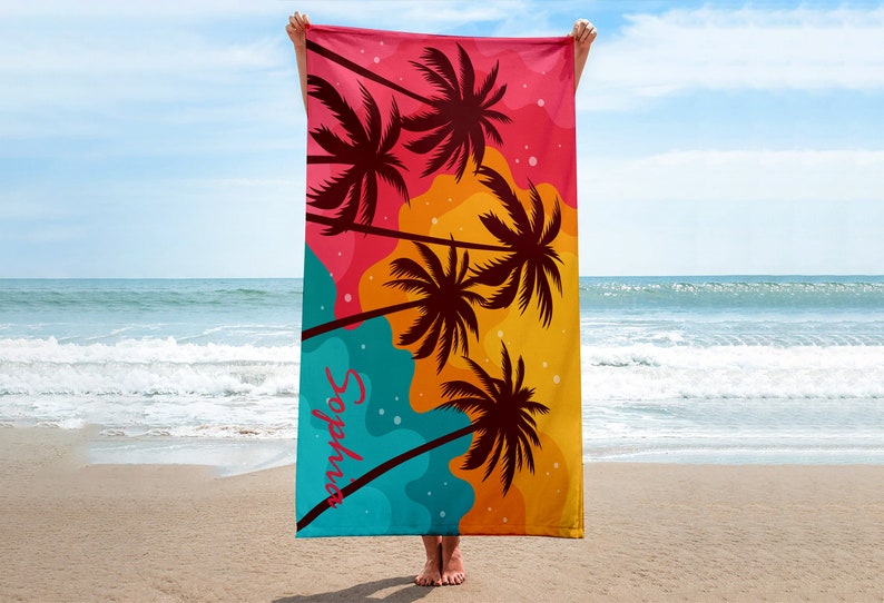 May include: A colourful beach towel with a tropical palm tree design. The towel is pink, orange, yellow, and blue with black palm trees. The text "Sophia" is printed on the towel.