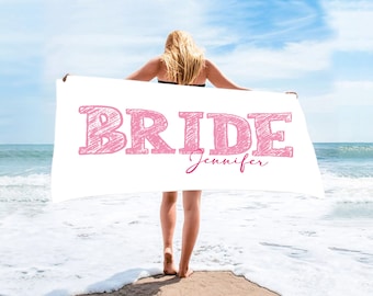 May include: White beach towel with the word "BRIDE" in pink script and the name "Jennifer" written below in pink script.