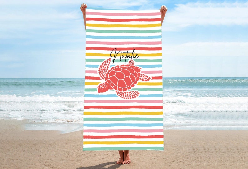 Puede incluir: Una toalla de playa colorida con una tortuga marina roja y el nombre Natalie impreso en ella. La toalla tiene rayas de arco&iacute;ris.