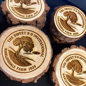 May include: Four wooden disc golf awards with bark edges. Each award is engraved with "The Sweet 5-0 Invitational" and "Harlinsdale Farm 2025". One reads "Team Champion", another "Closest to Pin", and a third "Overall Champion".