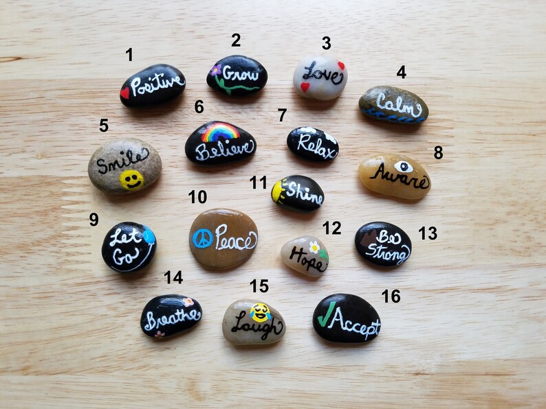 May include: A set of 16 painted rocks with positive affirmations, such as "Positive", "Grow", "Love", "Calm", "Smile", "Believe", "Relax", "Aware", "Let Go", "Peace", "Shine", "Hope", "Be Strong", "Breathe", "Laugh", and "Accept".