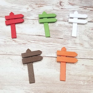 May include: Five wooden double-sided arrow signs in different colors: red, green, white, brown, and orange. The signs are all the same size and shape, and they are arranged in a row on a white wooden surface.