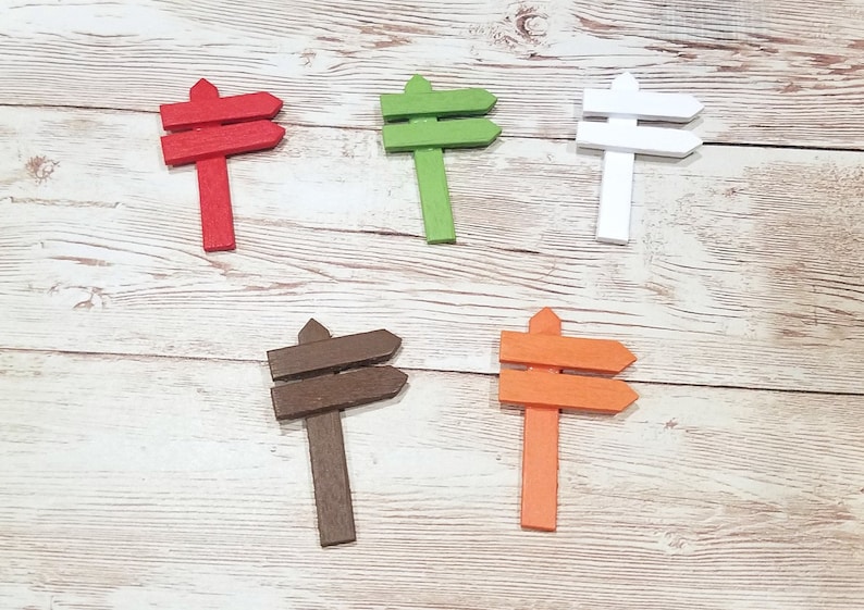 May include: Five wooden double-sided arrow signs in different colors: red, green, white, brown, and orange. The signs are all the same size and shape, and they are arranged in a row on a white wooden surface.