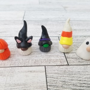 Op de afbeelding: Vijf Halloween-thema gnomen gemaakt van polymer clay. De gnomen zijn verkleed als een pompoen, een zwarte kat, een heks, een snoepstok en een spook.