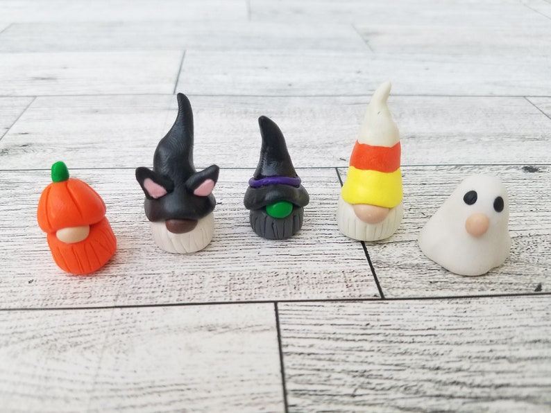 Op de afbeelding: Vijf Halloween-thema gnomen gemaakt van polymer clay. De gnomen zijn verkleed als een pompoen, een zwarte kat, een heks, een snoepstok en een spook.
