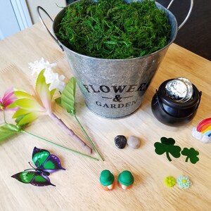 May include: A craft project with a variety of items including a metal bucket with the words "Flower & Garden" on it, a pot of gold, a rainbow, a butterfly, flowers, and small green shamrocks.