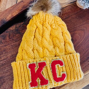 Kansas City Chiefs inspired cable knit Beanie in golden yellow with red KC Chenille Patch Letters on the folded cap line.
