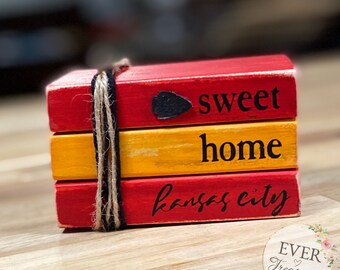May include: Stacked wooden blocks painted red and yellow with the words "sweet home kansas city" and a small black arrow.