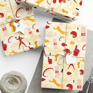 May include: Yellow and red wrapping paper with a football theme. The paper features a variety of football-related images, including footballs, helmets, and players. The paper also includes the letters "KC" repeated throughout the design.