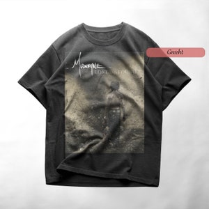Puede incluir: Una camiseta gris oscura con una imagen descolorida de una persona caminando de espaldas a la cámara. La imagen es del álbum "Lost and Found" de la banda Mudvayne.