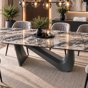 May include: A dining table featuring a large, glossy, multi-toned grey and white marble-patterned top with rounded edges. The table is supported by a singular, sculptural, matte dark grey base that curves underneath the centre of the tabletop.