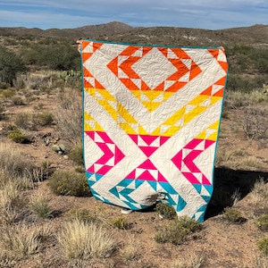May include: A colorful quilt with a geometric pattern in shades of orange, yellow, pink, turquoise, and white. The quilt is made with a variety of fabrics and is quilted with a simple stitch.