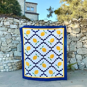 May include: A blue and white quilt with a lemon pattern. The quilt is made with yellow, green, and white fabric. It is displayed against a stone wall.