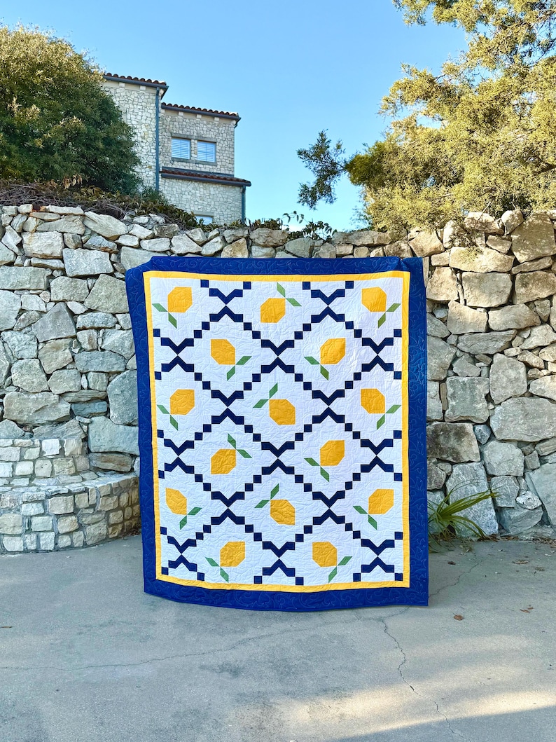May include: A blue and white quilt with a lemon pattern. The quilt is made with yellow, green, and white fabric. It is displayed against a stone wall.