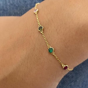May include: A gold chain bracelet with five colorful gemstones. The gemstones are green, pink, dark green, and red.