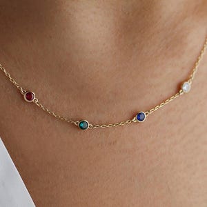 May include: A gold chain necklace with four small round gemstones: red, green, blue, and white.